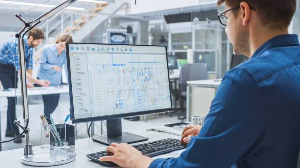 istock Over the Shoulder Shot of Engineer Working with CAD Software on Desktop Computer, Screen Shows Technical Drafts and Drawings. In the Background Engineering Facility Specialising on Industrial Design 1176842842