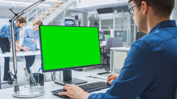 istock Over the Shoulder Shot of Engineer Working with Green Mock-up Screen Desktop Computer. In the Background Engineering Facility with Specialists Working on Blueprints and Drawings with Industrial Design 1176842855