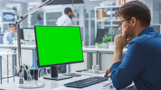 istock Over the Shoulder Shot of Engineer Working with Green Mock-up Screen Desktop Computer. In the Background Engineering Facility with Specialists Working on Blueprints and Drawings with Industrial Design 1176842891