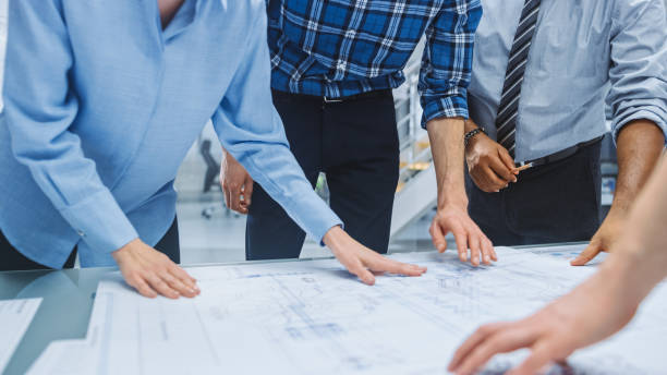 istock In the Industrial Engineering Facility: Diverse Group of Engineers and Technicians on a Meeting Gather Around Table Unravel Sheets of Engine Design Technical Drafts, Have Discussion, Analyse Drawings 1176842933
