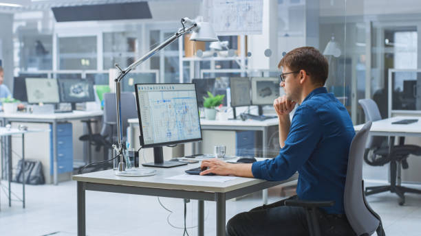 istock Over the Shoulder Shot of Engineer Working with CAD Software on Desktop Computer, Screen Shows Technical Drafts and Drawings. In the Background Engineering Facility Specialising on Industrial Design 1176842934