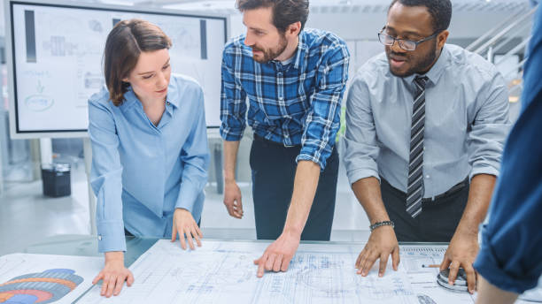 istock In the Industrial Engineering Facility: Diverse Group of Engineers and Technicians on a Meeting Gather Around Table Unravel Sheets of Engine Design Technical Drafts, Have Discussion, Analyse Drawings 1176842976