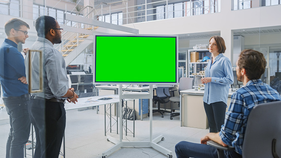 In the In Industrial Design Facility Team of Engineers and Technicians have a Meeting, Female Specialist Leads Briefing, Talks and Use Digital Interactive Whiteboard with Green Mock-up Screen