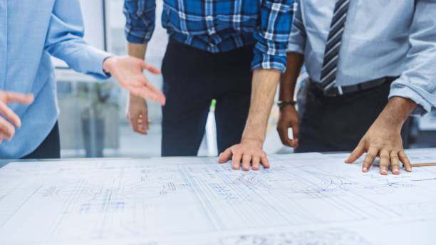 istock In the Industrial Engineering Facility: Diverse Group of Engineers and Technicians on a Meeting Gather Around Table Unravel Sheets of Engine Design Technical Drafts, Have Discussion, Analyse Drawings 1176843563
