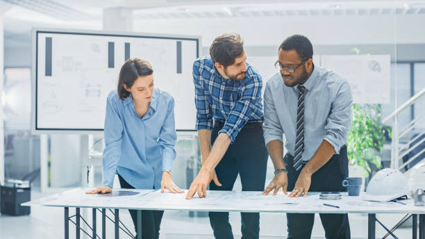 istock In the Industrial Engineering Facility: Diverse Group of Engineers and Technicians on a Meeting Gather Around Table Unravel Sheets of Engine Design Technical Drafts, Have Discussion, Analyse Drawings 1176843569