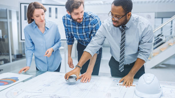 istock In the Industrial Engineering Facility: Diverse Group of Engineers and Technicians on a Meeting Gather Around Table Unravel Sheets of Engine Design Technical Drafts, Have Discussion, Analyse Drawings 1176843591