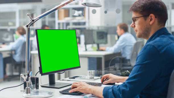 istock Over the Shoulder Shot of Engineer Working with Green Mock-up Screen Desktop Computer. In the Background Engineering Facility with Specialists Working on Blueprints and Drawings with Industrial Design 1176843626