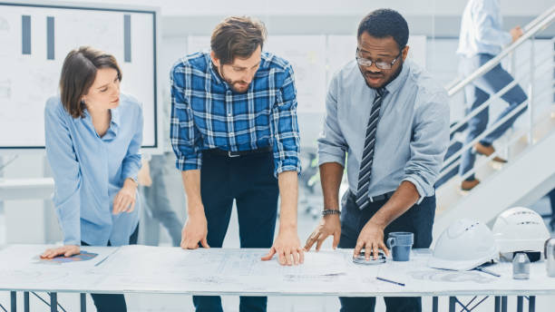 istock In the Industrial Engineering Facility: Diverse Group of Engineers and Technicians on a Meeting Gather Around Table Unravel Sheets of Engine Design Technical Drafts, Have Discussion, Analyse Drawings 1176843652