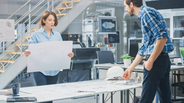 istock In the Industrial Engineering Facility: Female Architect Prints Drafts of Industrial Engine Prototype and Brings Them to Chief Engineer, Start Discussion and Analysis Using Conference Table. 1176843768