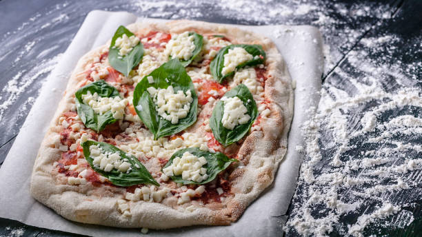 Raw Pizza Marguerite with basil on a cutting board. Close-up. Horizontal shot