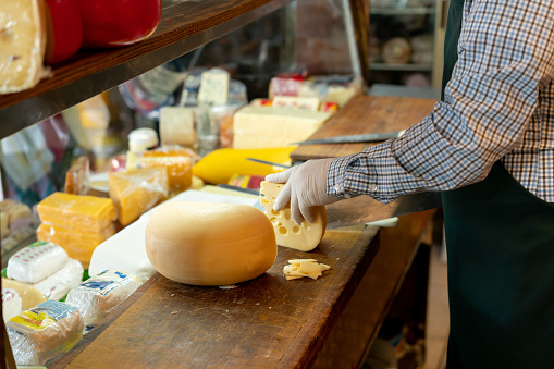 Unrecognizable man cutting cheese at a delicatessen  - Small business concepts