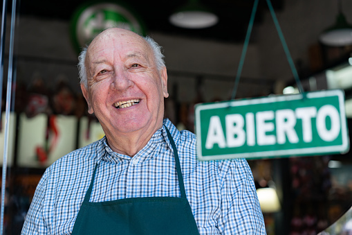 Senior business owner of a delicatessen opening for service smiling at camera very happy - Small business concepts