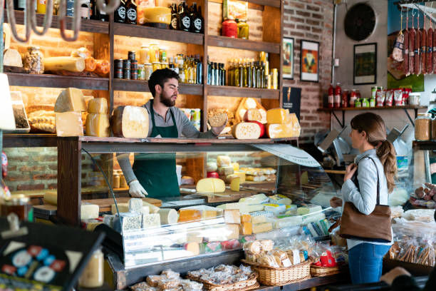 homme latino-américain travaillant à une épicerie fine suggeting un type de fromage à la cliente femelle - production locale photos et images de collection