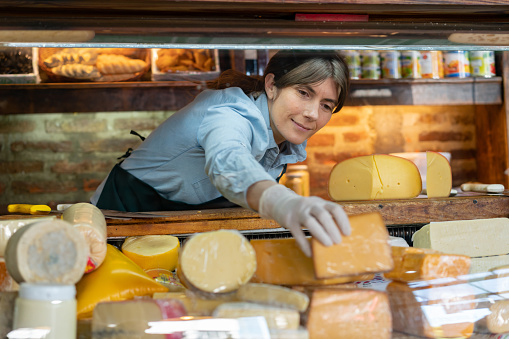 Beautiful business owner of a delicatessen arranging the cheese display - Small business concepts