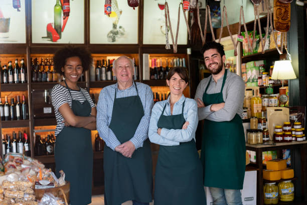 diverse team of sales people and business owner of a delicatessen wearing an apron smiling at camera - wine bottle liquor store wine variation imagens e fotografias de stock