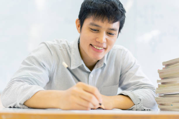 close up high school student man hand writing by mark  choices on answer sheet paper for final examination test in classroom concept