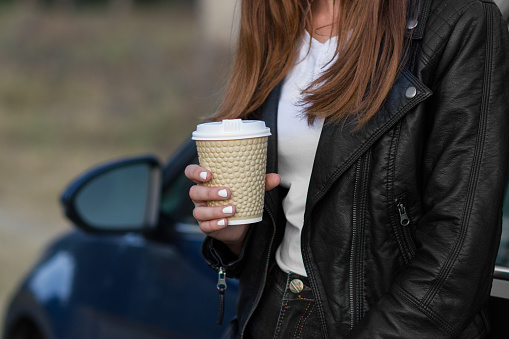 Girlwith hot cup of tea or coffee near a car.