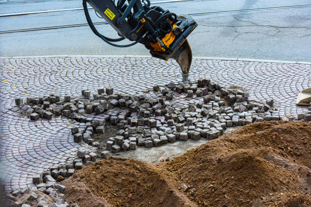 Excavator using a ripper tooth to remove cobblestones in the street.