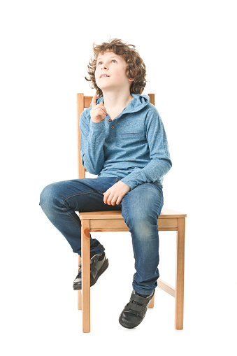 full length picture of curly 9 years old boy sitting on chair and thinking