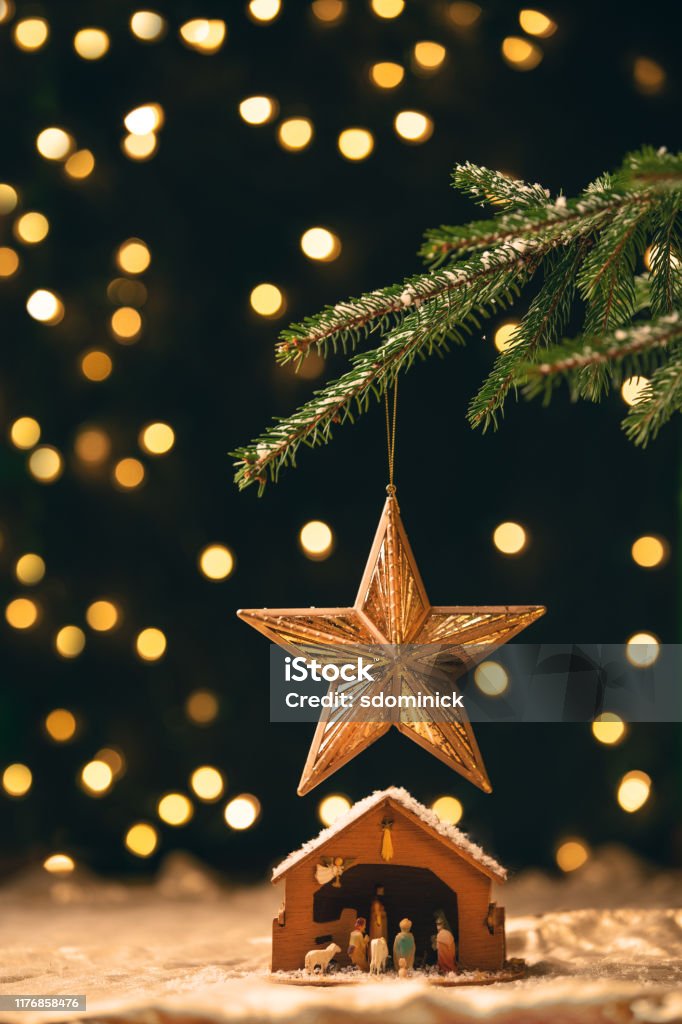 Manger Under a Christmas Tree A manger sitting under a star ornament that is hanging from a Christmas tree with lights blurred behind. Nativity Scene Stock Photo