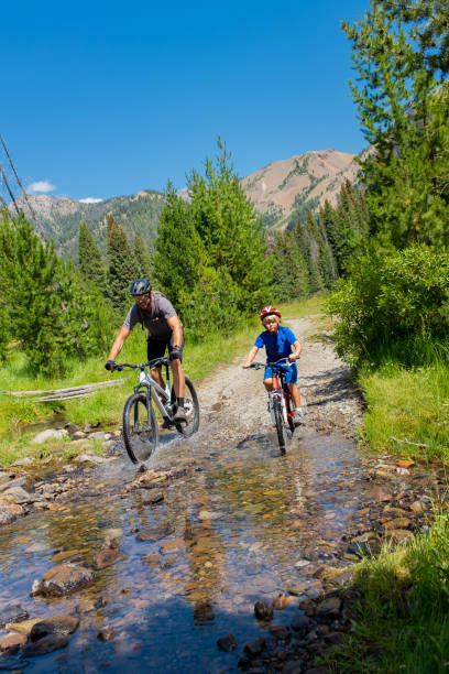 dad and 7 year old son riding through a creek in the mountains - sun valley idaho stock-fotos und bilder