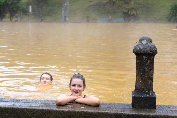 Teen girl and young adult man n a mineral thermal pool in the Terra Nostra park at Furnas, Sao Miguel island, Azores, Portugal. stock photo