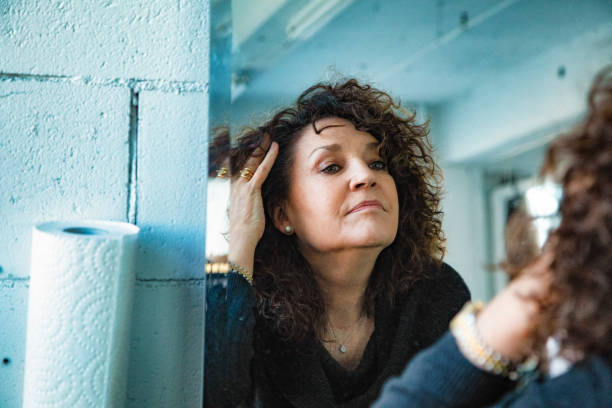 Mirror image of a pensive senior woman looking at her aging face Mirror image of a pensive senior woman looking at her aging face with a little sadness. chin stock pictures, royalty-free photos & images