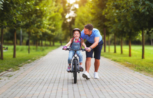 felice padre di famiglia insegna figlia bambino a andare in bicicletta nel parco - 11900 foto e immagini stock