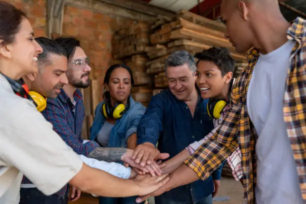 Group of Latin American workers at a wood factory putting their hands together while smiling - labor union concepts