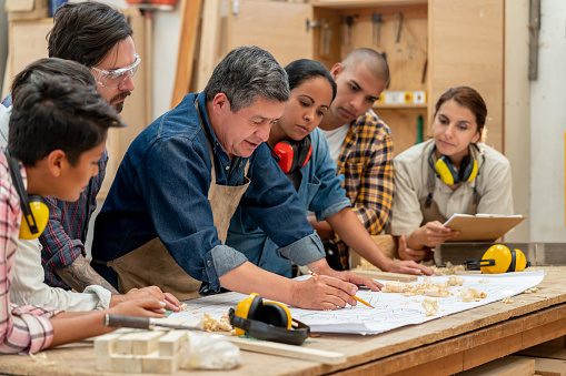 Group of Latin American workers at a factory making furniture and looking at a blueprint - manufacturing concepts