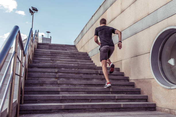 Athlete man runs in summer in city on steps, morning run, free space for text motivation fitness workout in fresh air. Jumping view from back. Sportswear shorts T-shirt Sneakers. stock photo