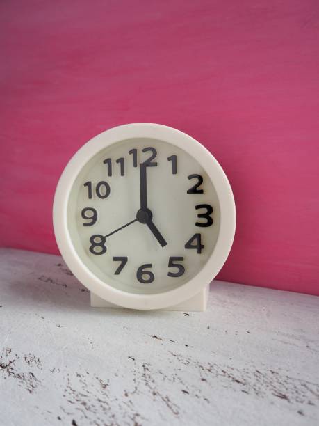 istock White clock pointing to 5 o'clock with white and pink painted wooden background 1176912663