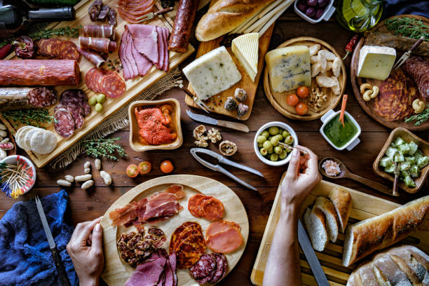 istock Female hands preparing snacks and appetizers in a set full of assorted Cured ham and cheese on rustic wood 1176912832