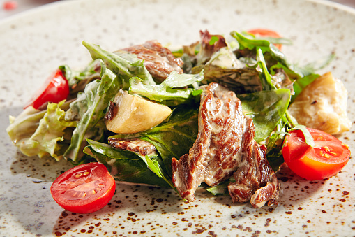 Warm salad with veal and porcini mushrooms in cream sauce. Vertical photo of roasted meat and mushroom salat with beef fillet, cherry tomatoes, arugula and fried boletus