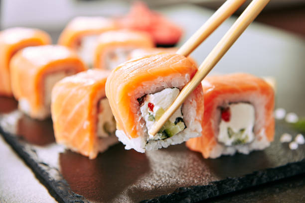 연어와 크림 치즈와 오이 와 함께 설정 스시 롤을 들고 젓가락 블랙 슬레이트 접시 닫아. 우라마키, 노리 마키 또는 송어 필레, 간장, 와사비를 곁들인 후토마키 스시 - sushi 뉴스 사진 이미지
