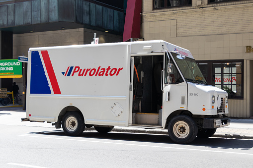 A Purolator Inc. delivery truck stopped on the side on a street in downtown Toronto on a sunny afternoon, seen with a door left open as the driver makes delivery on foot.
