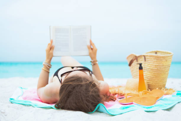 istock middle age woman on white beach reading book while laying 1176935166