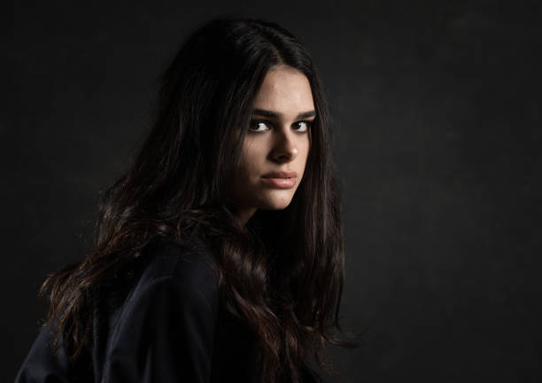 Studio portrait of a beautiful young teenage girl with very long hair wearing a black dress with a big white collar isolated against a grey background.