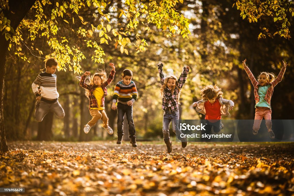 Verspielte kleine Freunde, die Spaß beim Springen im Herbsttag im Park haben. - Lizenzfrei Kind Stock-Foto