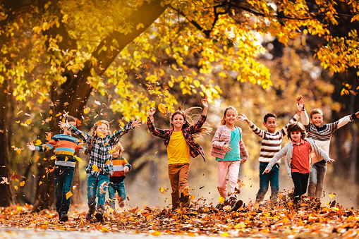 Large group of happy kids having fun while running through autumn leaves in the park. Copy space.