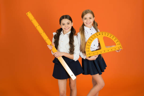 istock Education and school concept. School students learning geometry. Kids school uniform on orange background. STEM school disciplines. Pupil cute girls with big rulers. Geometry favorite subject 1176958781
