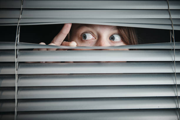 istock Terrified young woman stares sideways through blinds 1176958977