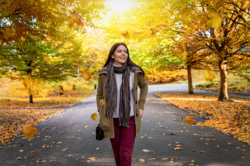 A attractive woman walks in a autumn park in the city with golden leaves and sunshine