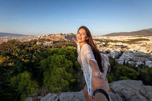 A beautiful traveler woman pulls her friend from the hand to the Acropolis of Athens, Greece, during their vacation time