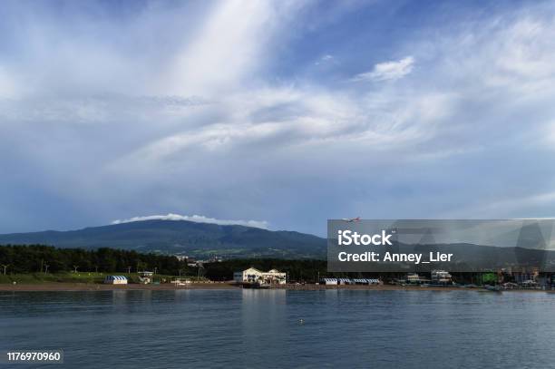 Airplane Flying Over Iho Tewoo Beach On Jeju Island With Hallasan Mountain And Scenic Cloudscape On Background Stock Photo - Download Image Now