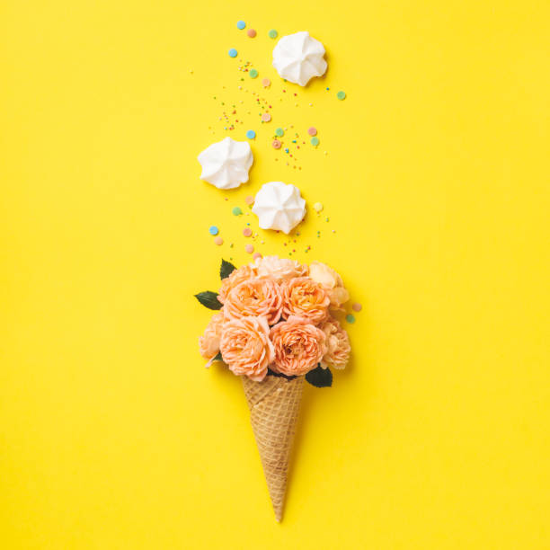 Ice cream cone with pink roses and merengues on yellow background. Summer minimal concept. Flat lay.