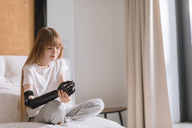 istock beautiful girl looking at her prosthetic arm while sitting on the bed 1176972999