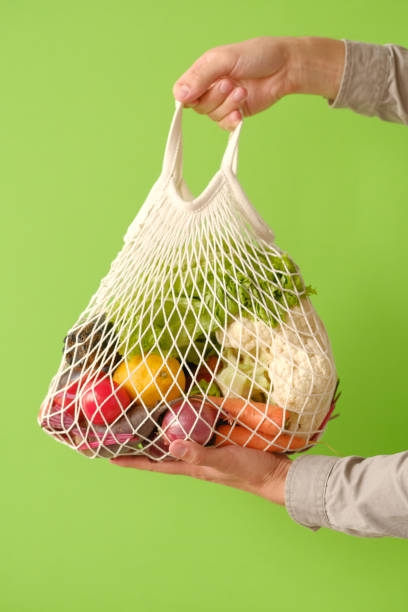 istock Male hand holding a white string shopping bag with vegetables on green background. Zero waste shopping concept. 1176976202