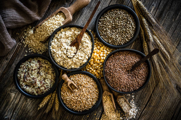 Large group of wholegrain food shot on rustic wooden table Top view of wholegrain and cereal composition shot on rustic wooden table. This type of food is rich of fiber and is ideal for dieting. The composition includes oat flakes, brown rice, dried corn,spelt, hemp seeds and flax seeds. Predominant color is brown. XXXL 42Mp studio photo taken with SONY A7rII and Zeiss Batis 40mm F2.0 CF oat wheat oatmeal cereal plant stock pictures, royalty-free photos & images