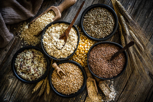Large group of wholegrain food shot on rustic wooden table Top view of wholegrain and cereal composition shot on rustic wooden table. This type of food is rich of fiber and is ideal for dieting. The composition includes oat flakes, brown rice, dried corn,spelt, hemp seeds and flax seeds. Predominant color is brown. XXXL 42Mp studio photo taken with SONY A7rII and Zeiss Batis 40mm F2.0 CF rice cereal plant stock pictures, royalty-free photos & images